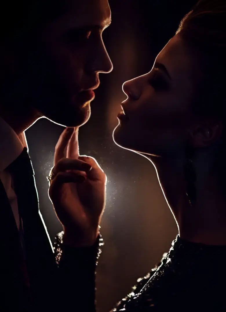 A well-dressed couple sharing a romantic moment, facing each other in dim light.